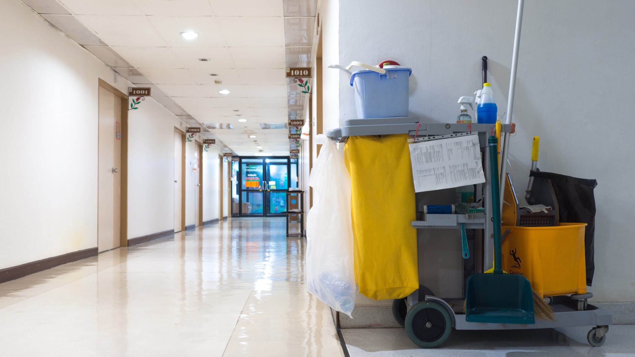 A cart covered in cleaning supplies is parked in a hospital hallway