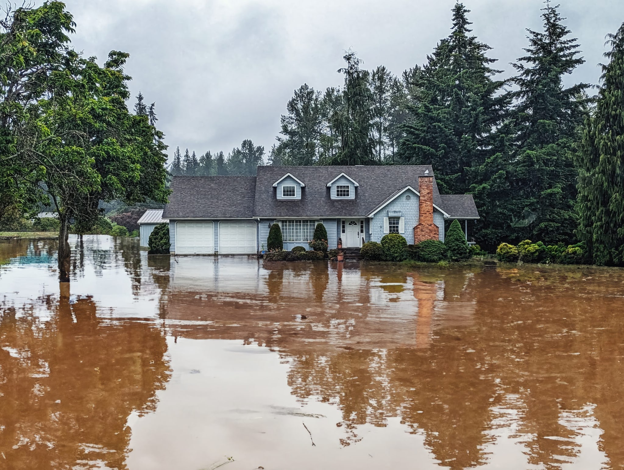 Deep floodwater around a house in a rural area after a natural disaster.