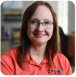 Woman wearing a coral-colored shirt with the letters O.P.D.H. and glasses.